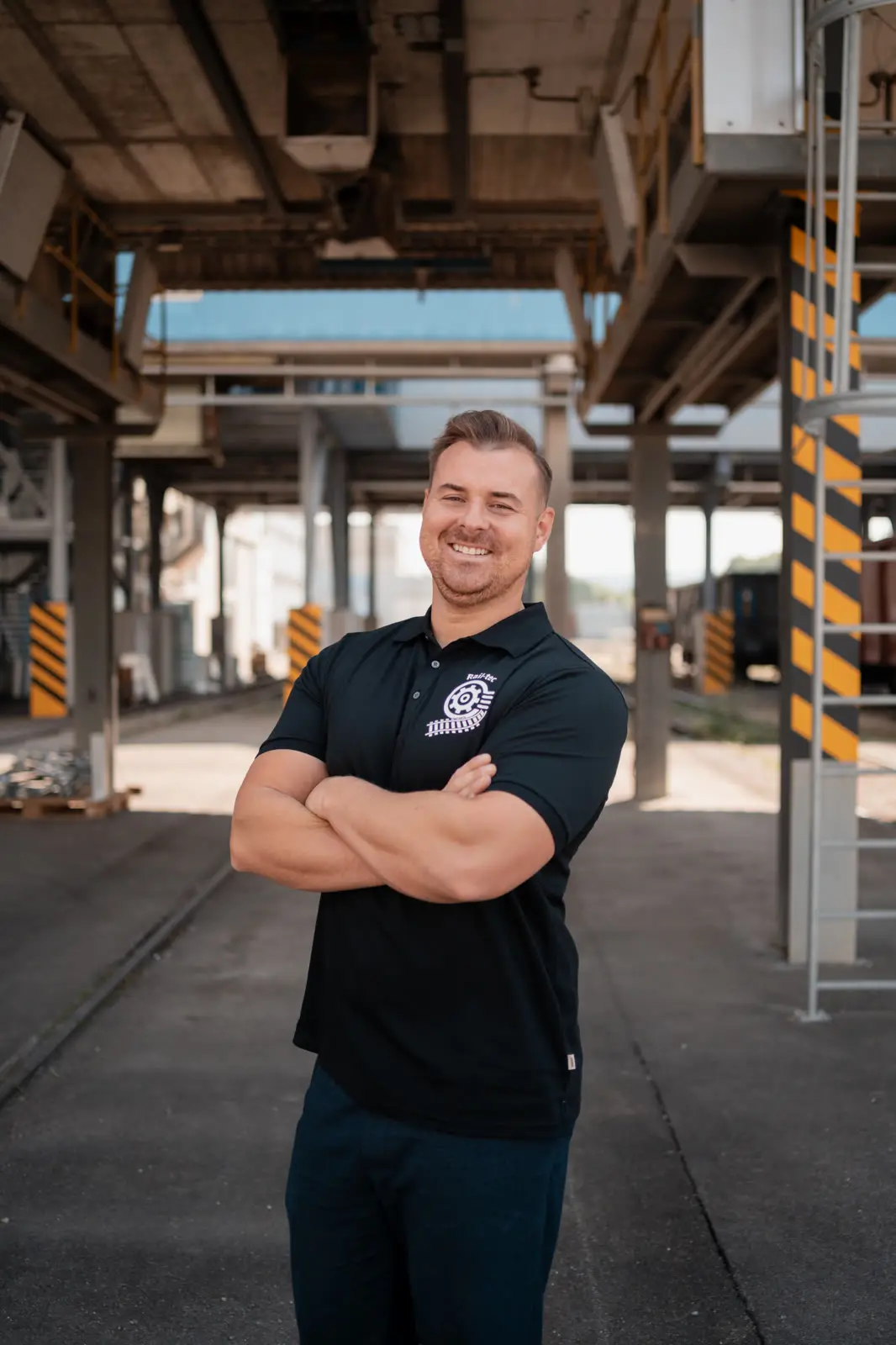 Ein Mitarbeiter von Rail-tec im Polohemd der Firma, unter dem Vordach einer Verladehalle.
